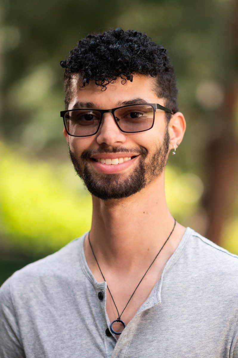 Smiling, bearded person with tinted glasses